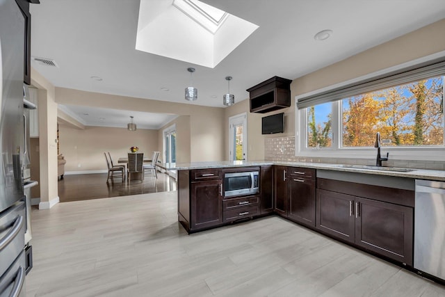 kitchen with a skylight, sink, pendant lighting, appliances with stainless steel finishes, and light wood-type flooring