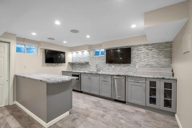 bar with decorative backsplash, light stone countertops, gray cabinetry, and sink