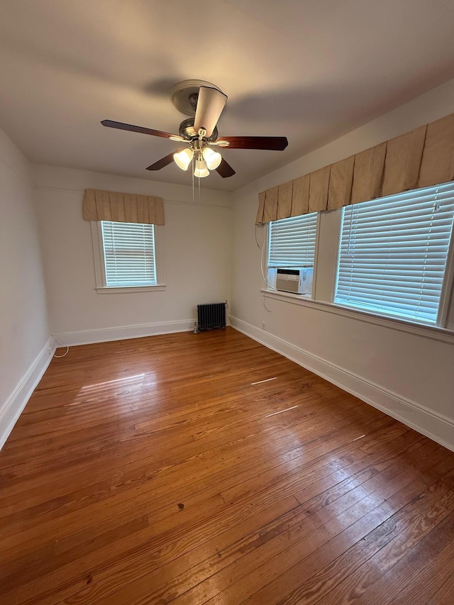 empty room featuring radiator heating unit, hardwood / wood-style floors, ceiling fan, and cooling unit