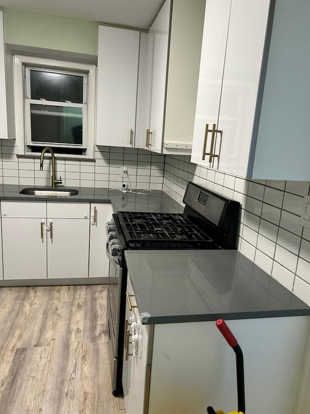 kitchen featuring sink, gas range, white cabinetry, tasteful backsplash, and light hardwood / wood-style floors