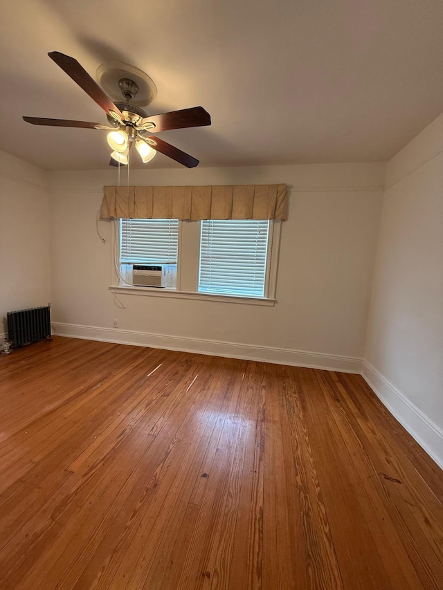 spare room with radiator, ceiling fan, cooling unit, a wealth of natural light, and wood-type flooring