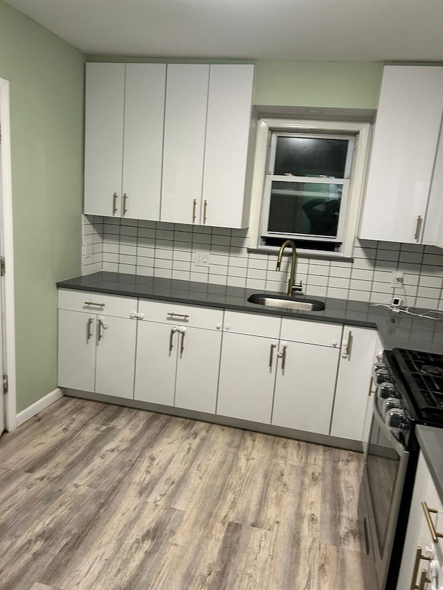 kitchen with stainless steel gas stove, white cabinetry, sink, decorative backsplash, and light hardwood / wood-style floors