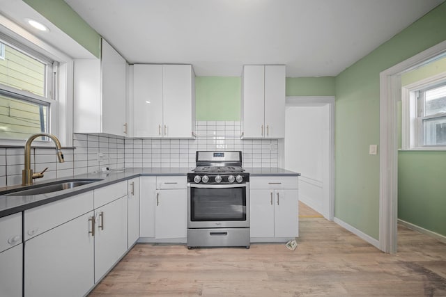 kitchen with white cabinetry, backsplash, sink, and stainless steel gas range oven