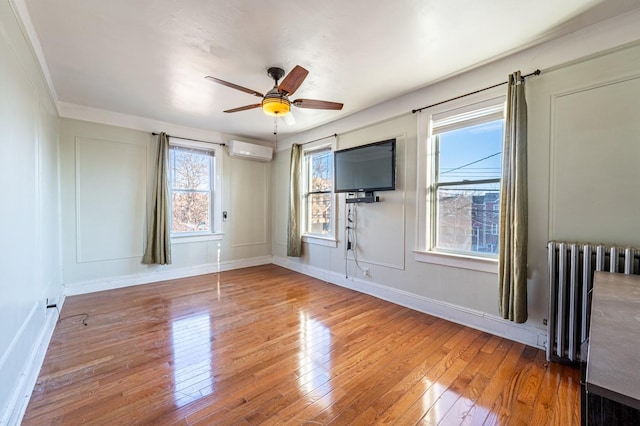 spare room featuring a wall mounted air conditioner, plenty of natural light, wood-type flooring, and radiator heating unit