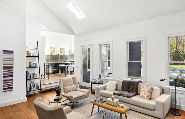 living room with light hardwood / wood-style floors, high vaulted ceiling, and a skylight