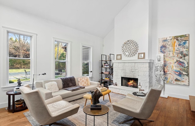 living room with a stone fireplace, high vaulted ceiling, and light hardwood / wood-style flooring