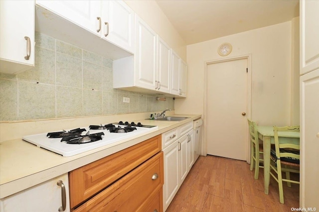 kitchen with decorative backsplash, white gas stovetop, sink, white cabinets, and light hardwood / wood-style floors