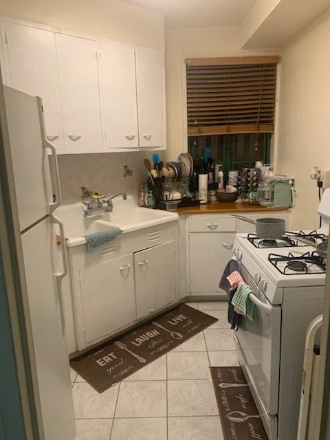 kitchen featuring decorative backsplash, white appliances, sink, white cabinetry, and light tile patterned flooring