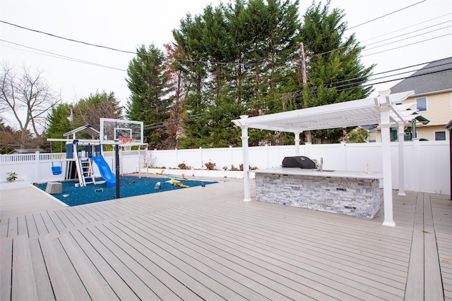 wooden deck featuring area for grilling, a pergola, a playground, and an outdoor kitchen