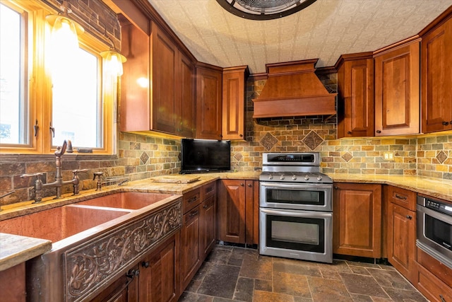 kitchen with sink, decorative backsplash, light stone countertops, custom range hood, and stainless steel appliances