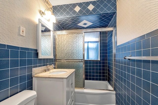 full bathroom with vanity, toilet, bath / shower combo with glass door, and tile walls