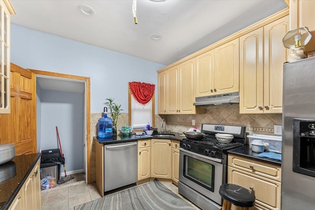 kitchen with sink, backsplash, dark stone counters, light tile patterned floors, and appliances with stainless steel finishes