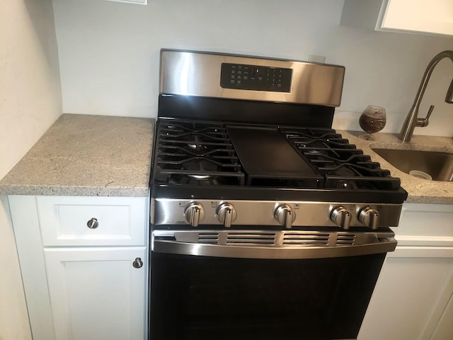 details featuring stainless steel gas stove, light stone countertops, white cabinetry, and sink