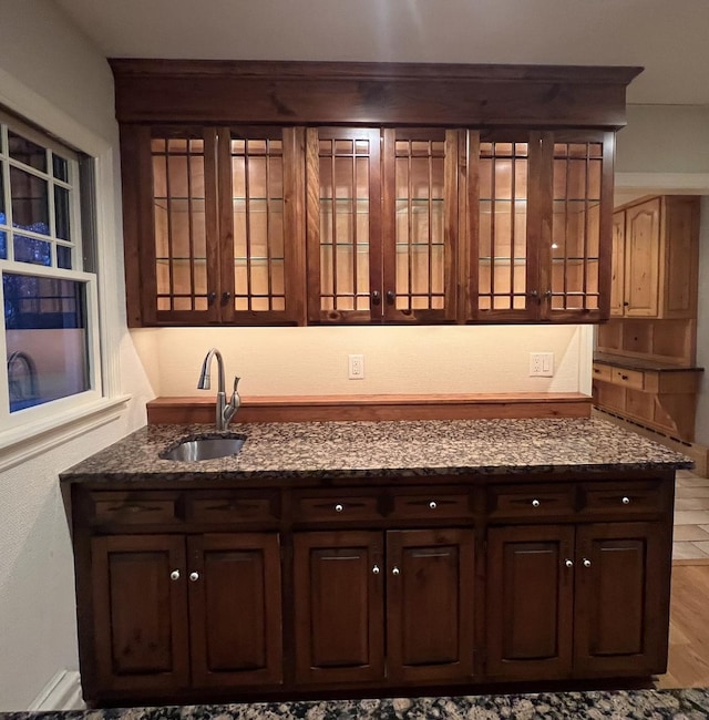 bar with dark brown cabinets, light hardwood / wood-style flooring, dark stone counters, and sink