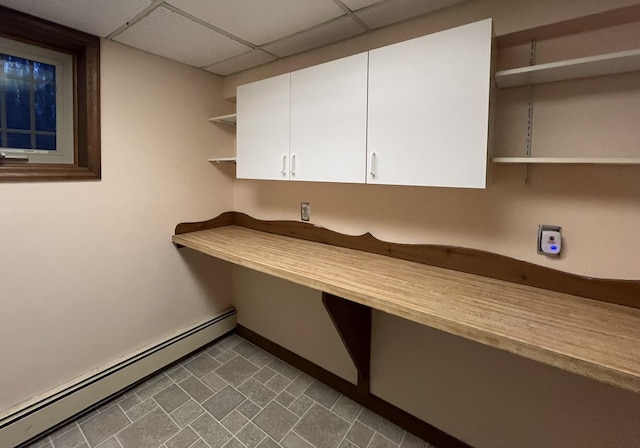 unfurnished office featuring a paneled ceiling, dark tile patterned flooring, and a baseboard heating unit