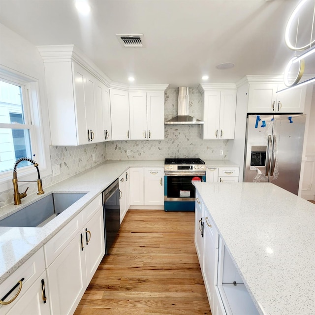 kitchen featuring light wood-type flooring, wall chimney exhaust hood, stainless steel appliances, sink, and decorative light fixtures