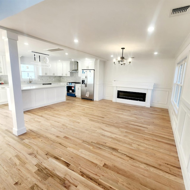 unfurnished living room with crown molding, sink, light hardwood / wood-style floors, and an inviting chandelier