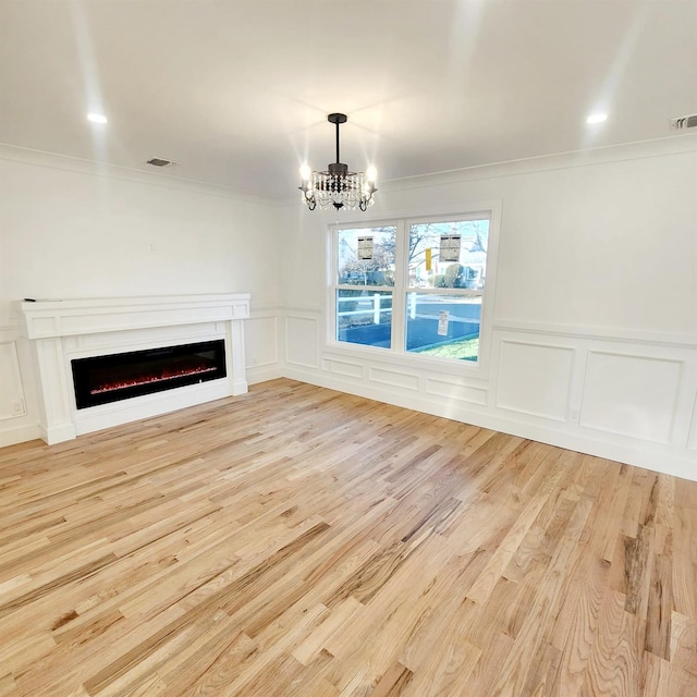 unfurnished living room featuring crown molding, light hardwood / wood-style floors, and an inviting chandelier