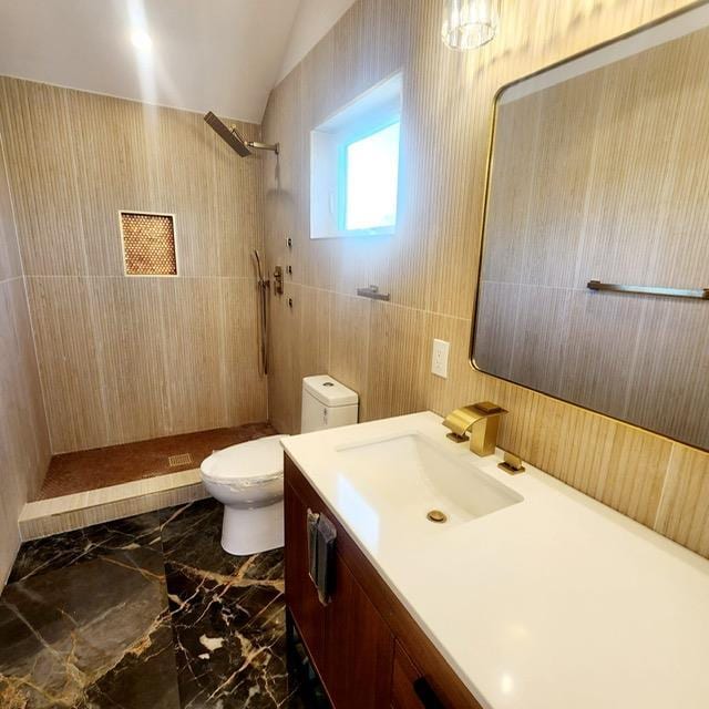 bathroom with a tile shower, vanity, vaulted ceiling, tile walls, and toilet