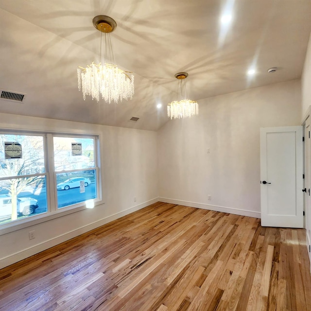 spare room with vaulted ceiling, wood-type flooring, and an inviting chandelier