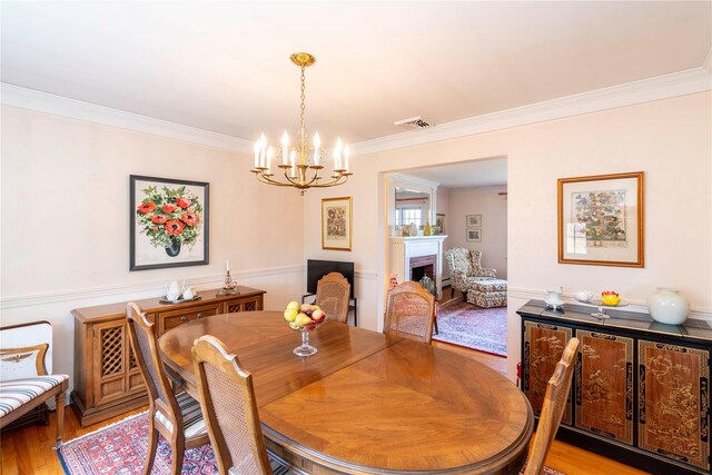 dining room with a fireplace, light wood-type flooring, crown molding, and a notable chandelier