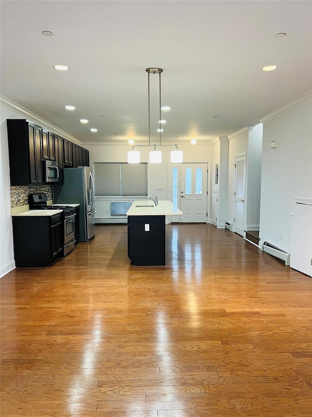 kitchen with a baseboard heating unit, stainless steel appliances, sink, hanging light fixtures, and a kitchen island with sink