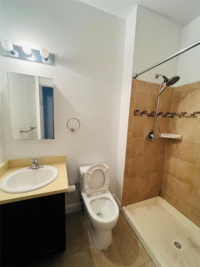 bathroom with toilet, vanity, a tile shower, and tile patterned flooring