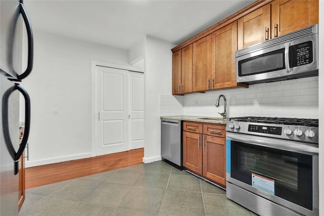 kitchen with light stone countertops, sink, stainless steel appliances, dark tile patterned floors, and decorative backsplash