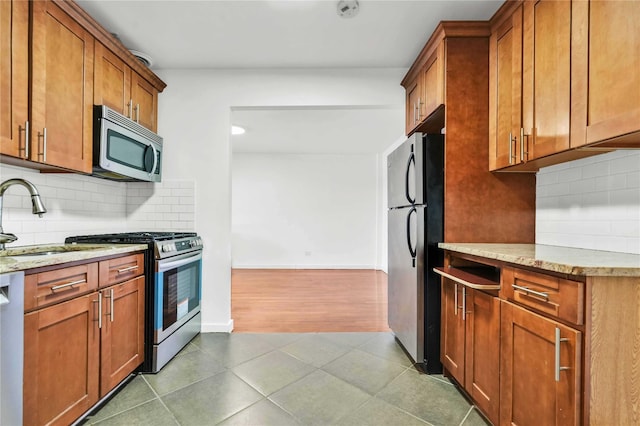 kitchen with backsplash, sink, light stone countertops, appliances with stainless steel finishes, and wood-type flooring