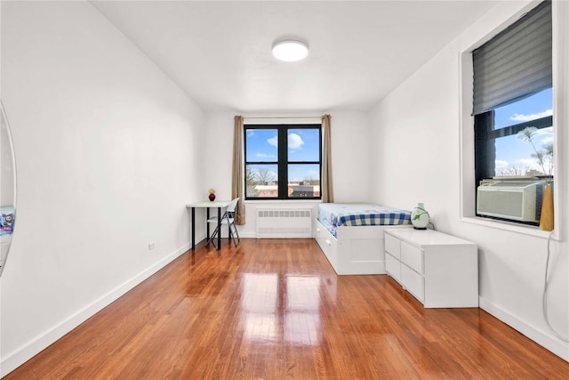 unfurnished bedroom featuring cooling unit, light hardwood / wood-style floors, radiator heating unit, and multiple windows