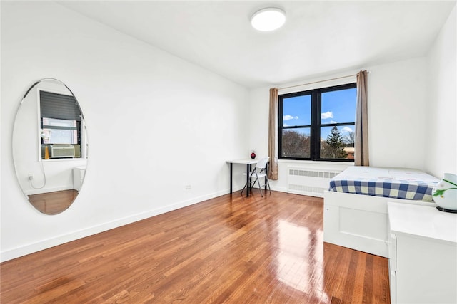 bedroom with radiator heating unit, cooling unit, and wood-type flooring