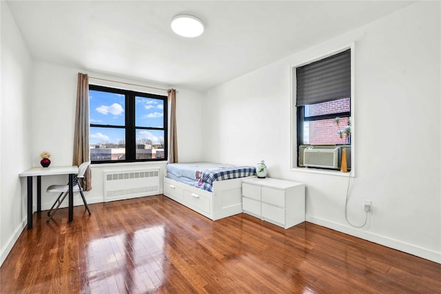 unfurnished bedroom featuring cooling unit, radiator heating unit, and dark wood-type flooring