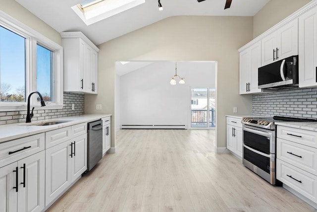 kitchen featuring stainless steel appliances, lofted ceiling with skylight, a baseboard heating unit, sink, and white cabinets