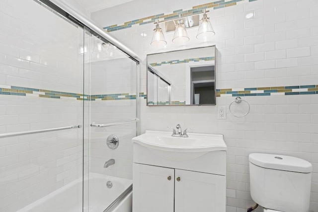 full bathroom featuring shower / bath combination with glass door, vanity, toilet, and tile walls