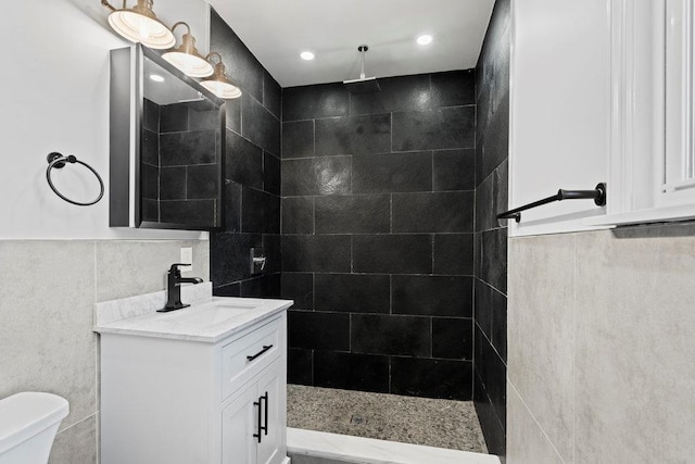 bathroom with a tile shower, vanity, tile walls, and toilet