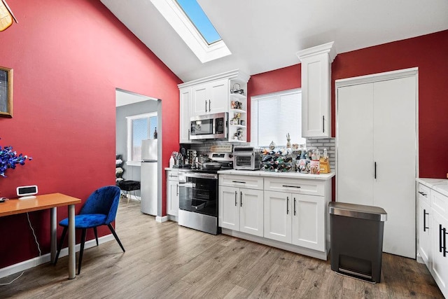 kitchen featuring white cabinetry, stainless steel appliances, tasteful backsplash, light hardwood / wood-style floors, and vaulted ceiling with skylight