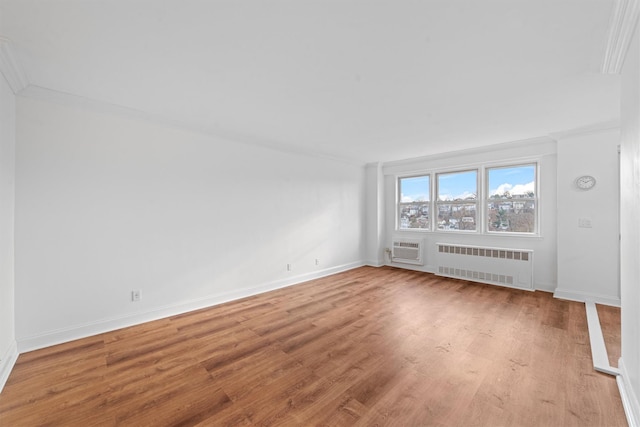 empty room featuring a wall unit AC, light wood-type flooring, ornamental molding, and radiator