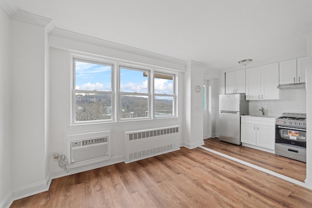 kitchen with white cabinets, an AC wall unit, light wood-type flooring, appliances with stainless steel finishes, and radiator heating unit