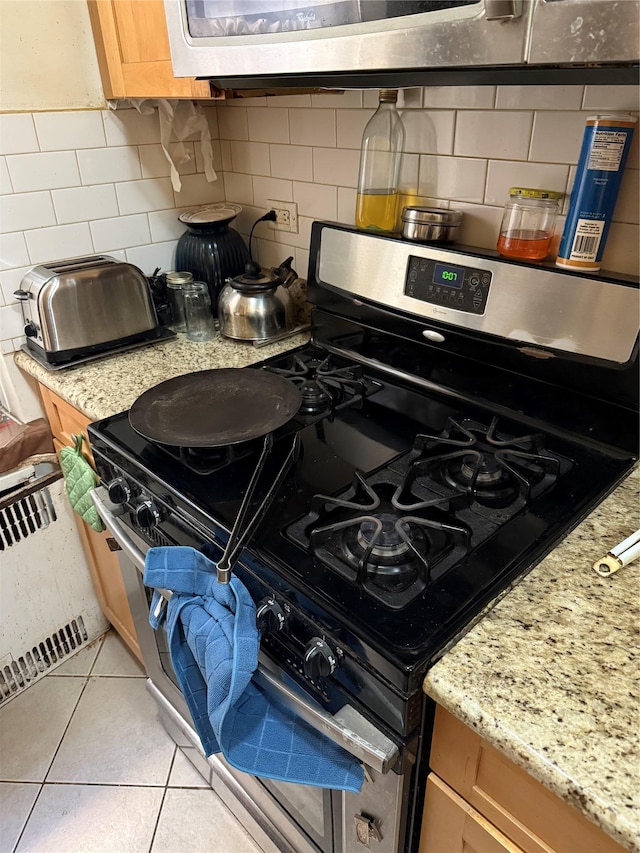 kitchen featuring light tile patterned flooring, black range with gas stovetop, light stone countertops, and backsplash