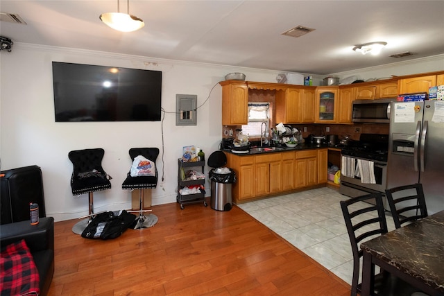 kitchen with appliances with stainless steel finishes, light wood-type flooring, ornamental molding, and sink