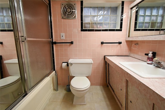 full bathroom featuring vanity, combined bath / shower with glass door, tile patterned flooring, toilet, and tile walls