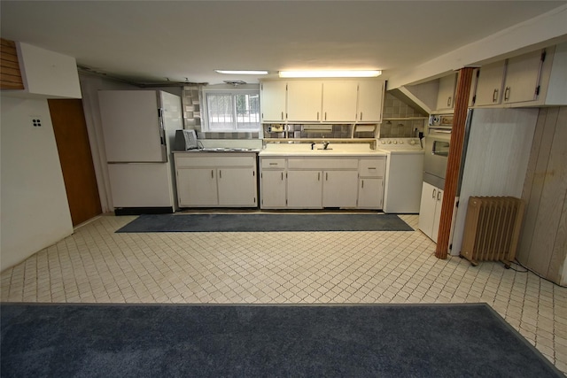 kitchen with sink, white refrigerator, washer / dryer, radiator heating unit, and white cabinetry