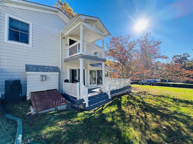 view of side of property featuring roof with shingles, a lawn, and a balcony