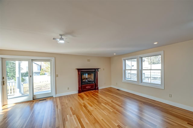 unfurnished living room with light wood-style floors, a glass covered fireplace, visible vents, and baseboards