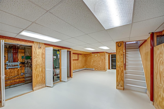 finished below grade area featuring stairs, a baseboard heating unit, a drop ceiling, and wooden walls