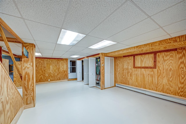 finished below grade area with wood walls, baseboards, a baseboard heating unit, and a drop ceiling