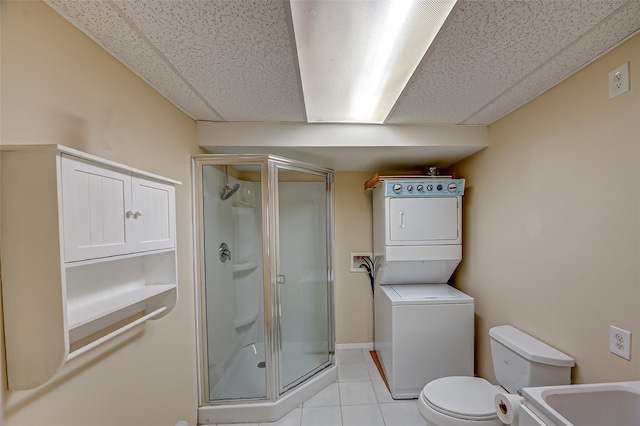 full bathroom featuring a stall shower, toilet, stacked washing maching and dryer, and tile patterned floors