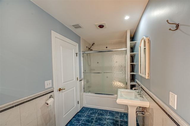 bathroom with a wainscoted wall, tile walls, visible vents, combined bath / shower with glass door, and tile patterned floors