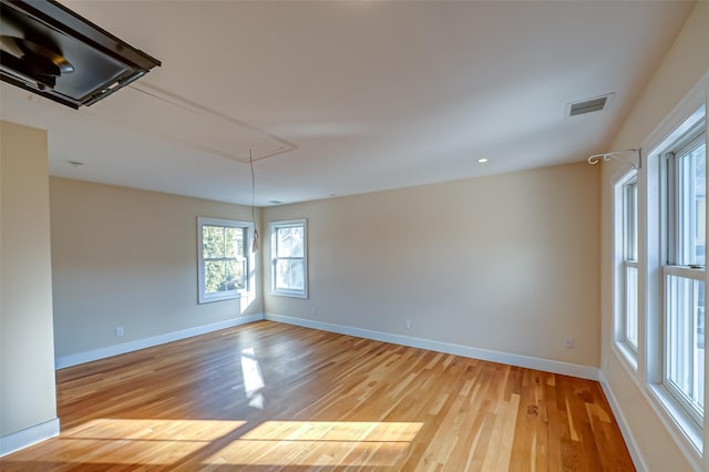 empty room with attic access, visible vents, light wood-style flooring, and baseboards