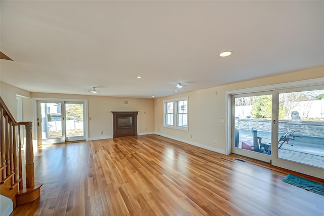 unfurnished living room featuring light wood finished floors, stairway, plenty of natural light, and a glass covered fireplace